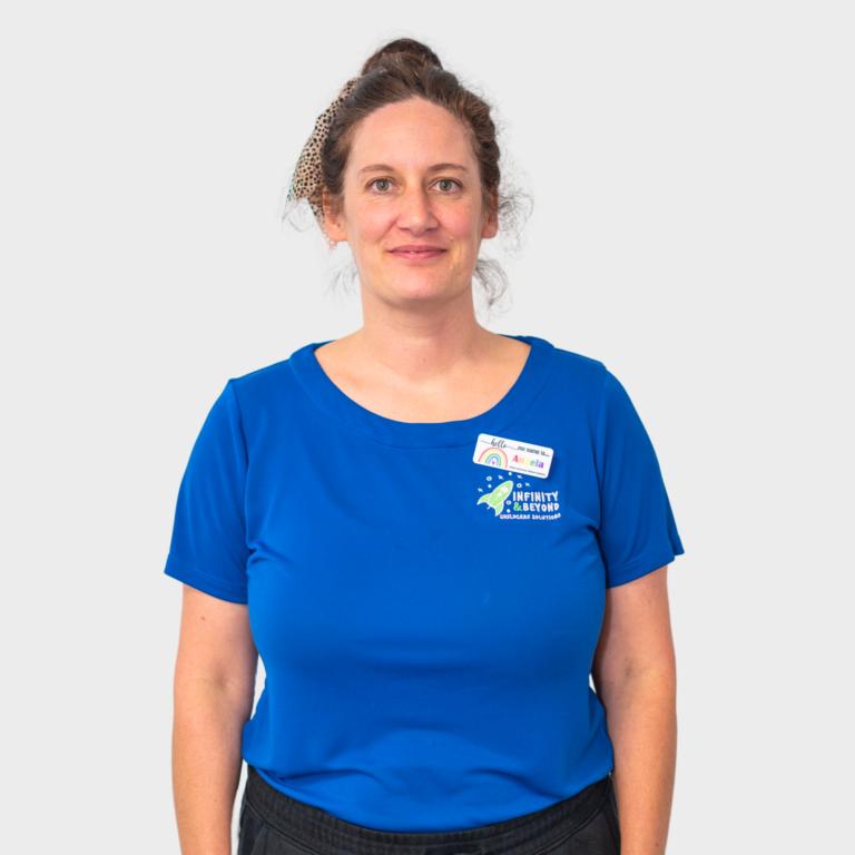 An early childhood educator with brown hair in a bun wearing a blue Infinity and Beyond Childcare Solutions shirt, smiling.