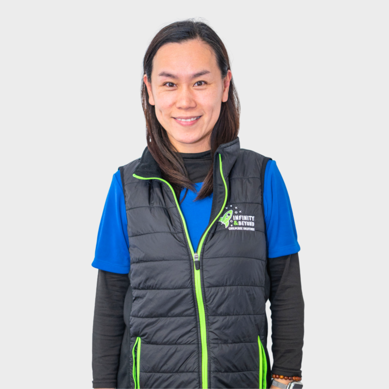 An early childhood educator with dark hair wearing a black vest with green accents and an Infinity and Beyond Childcare Solutions logo, smiling.