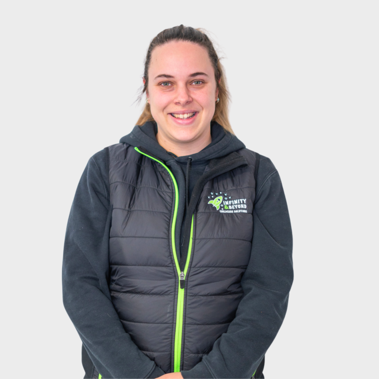 An early childhood educator with blonde hair in a ponytail wearing a black jacket with an Infinity and Beyond Childcare Solutions logo, smiling.