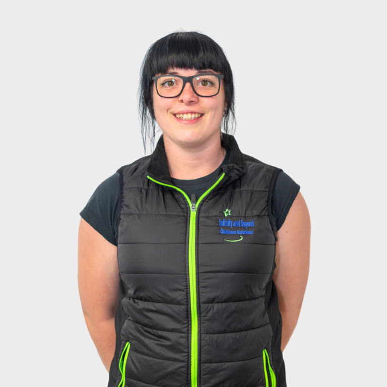 An early childhood educator with black hair and glasses wearing a black vest with green accents and an Infinity and Beyond Childcare Solutions logo, smiling.