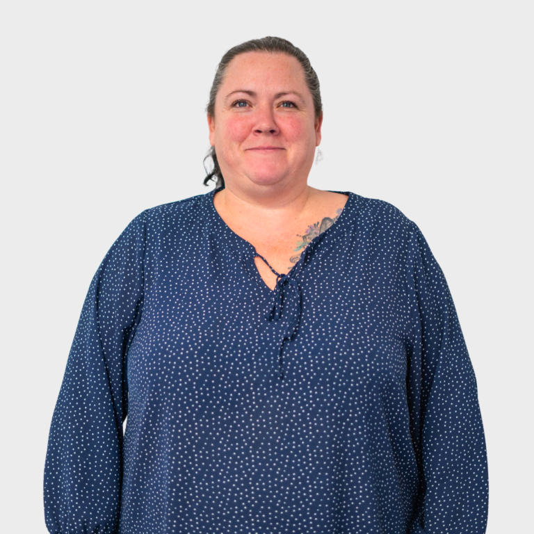 An early childhood educator with dark blonde hair in a bun wearing a blue polka-dot blouse, smiling.