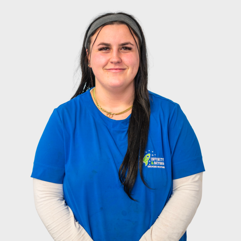 An early childhood educator with long dark hair wearing a blue Infinity and Beyond Childcare Solutions shirt, smiling.